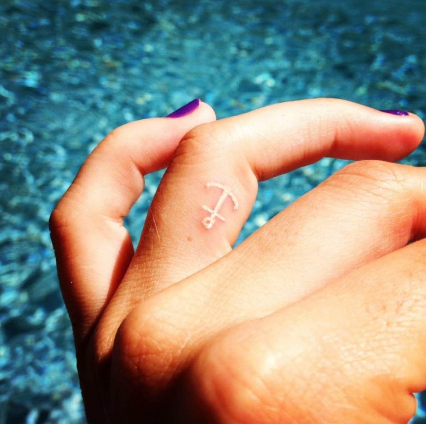 Tattoo created with white ink in the form of an anchor placed on the middle finger