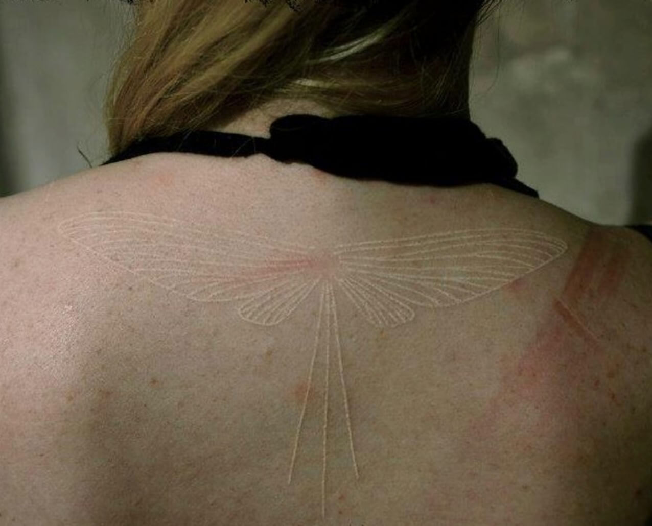 Back of a girl with a white ink tattoo that is a dragonfly