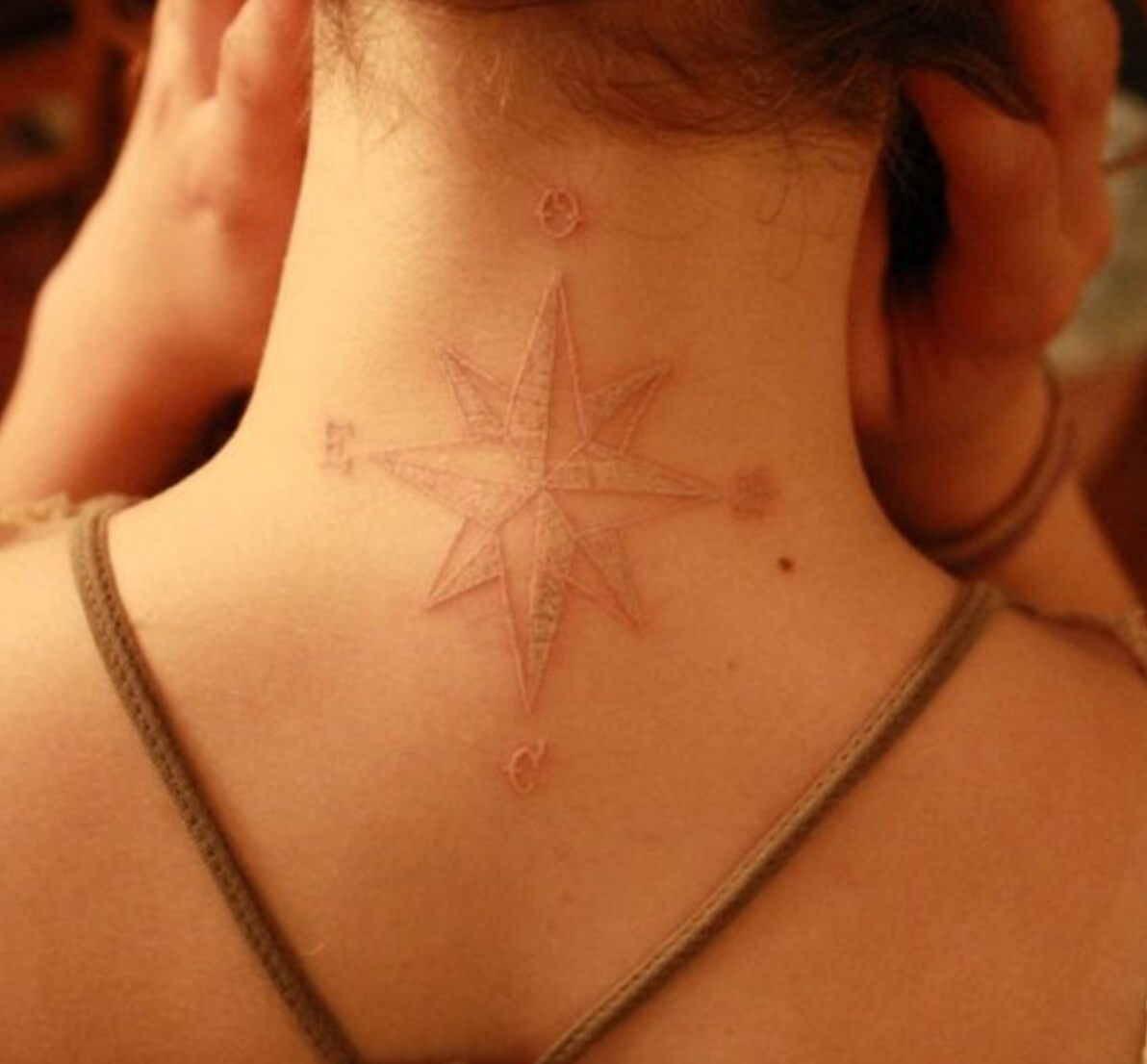 White ink tattoo in the form of a wind rose placed on the neck