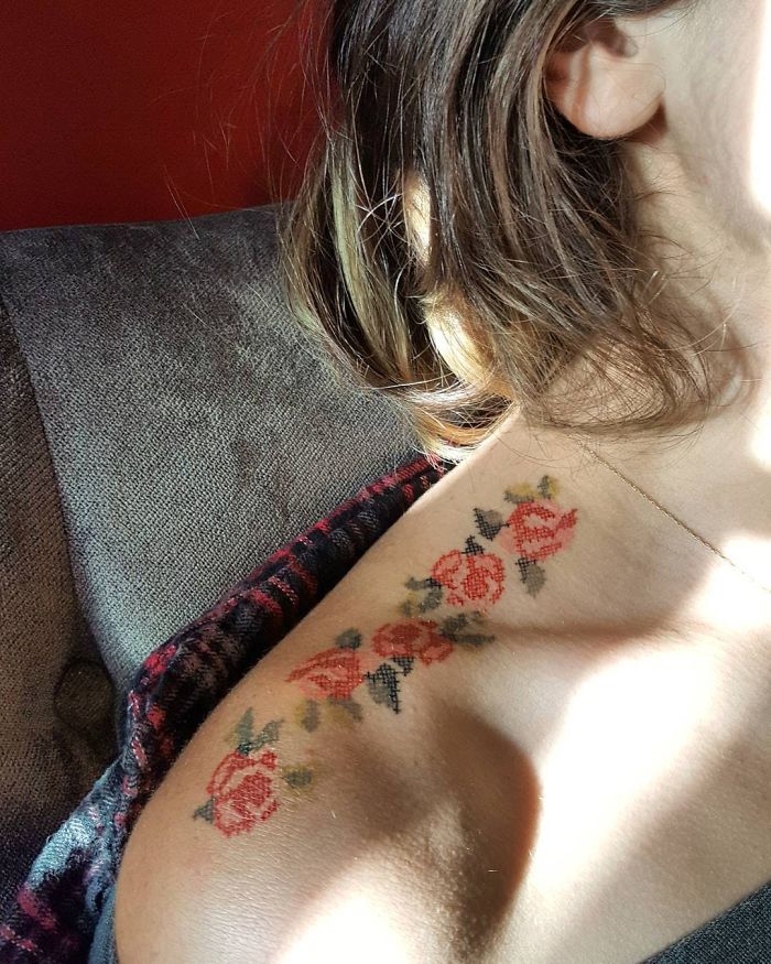 Girl lying on a sofa, showing her bare shoulder to show her roses guide tattoo with cross stitch embroidery effect