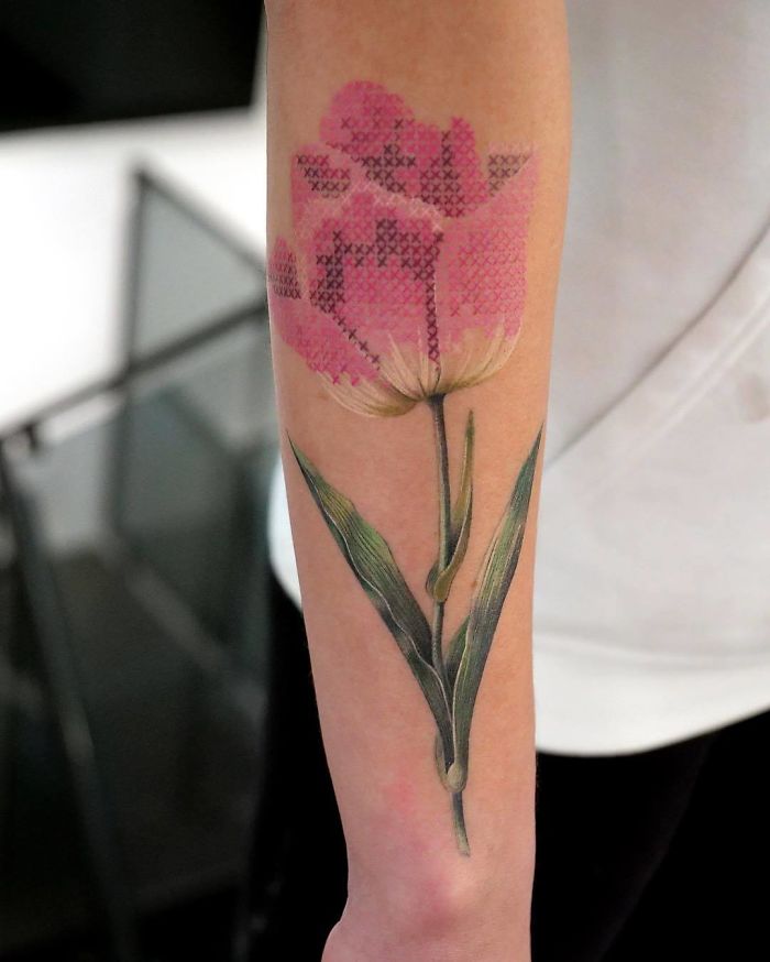 Person showing his forearm with a pink tulip tattoo with cross stitch embroidery effect