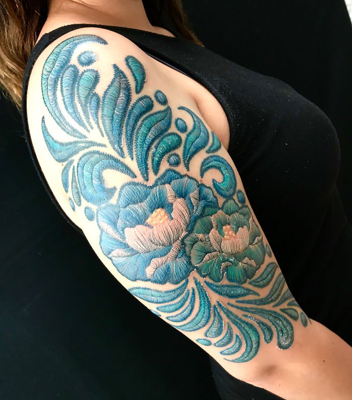 Girl standing in profile showing her right arm with a tattoo guides in blue with embroidery effect